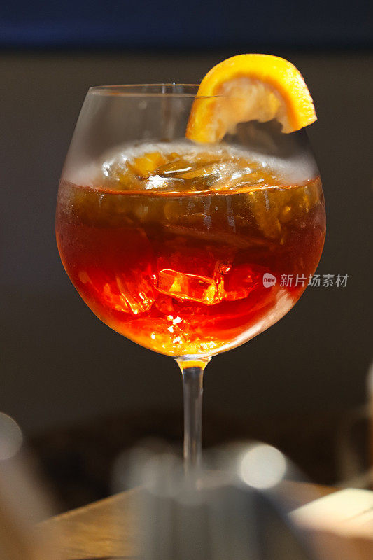 图片中，斯普利茨·威尼斯诺(Spritz Veneziano)鸡尾酒装在葡萄酒杯里，在木桌上装饰着橘子片，普罗赛克(Prosecco)、消化苦味酒、苏打水和冰块，用餐背景，重点放在前景上